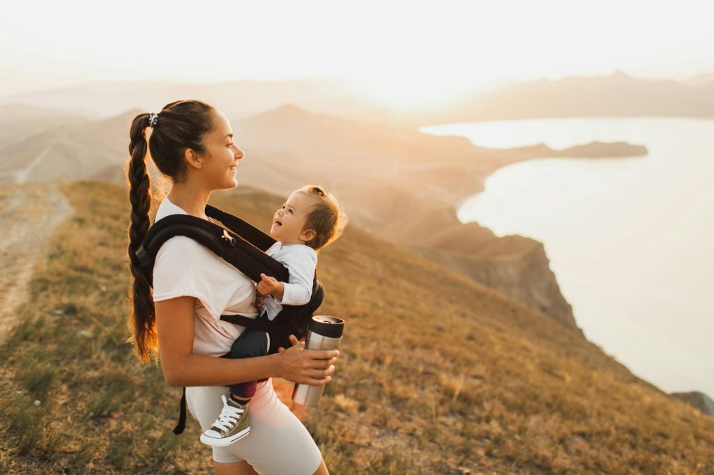 Voyager avec des enfants en bas âge : oui ou non ? Happy young woman travel and hike with toddler baby in sling. Active lifestyle