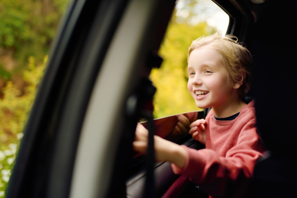 Cute preteen boy looking out through window of car during family road trip and enjoy