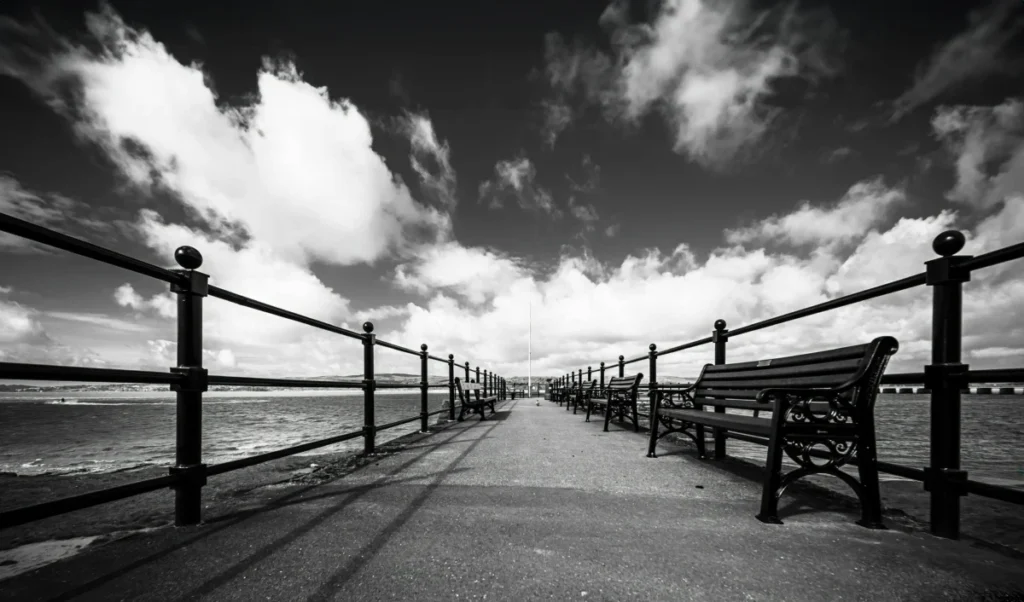 A stunning black and white view of Arnside promenade with benches and dramatic clouds overhead.