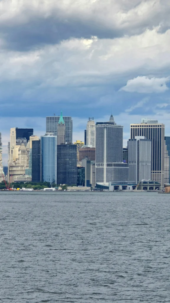 Prêt à plonger dans une nouvelle aventure ? Stunning view of New York City's skyline with prominent skyscrapers and waterfront on a cloudy day.