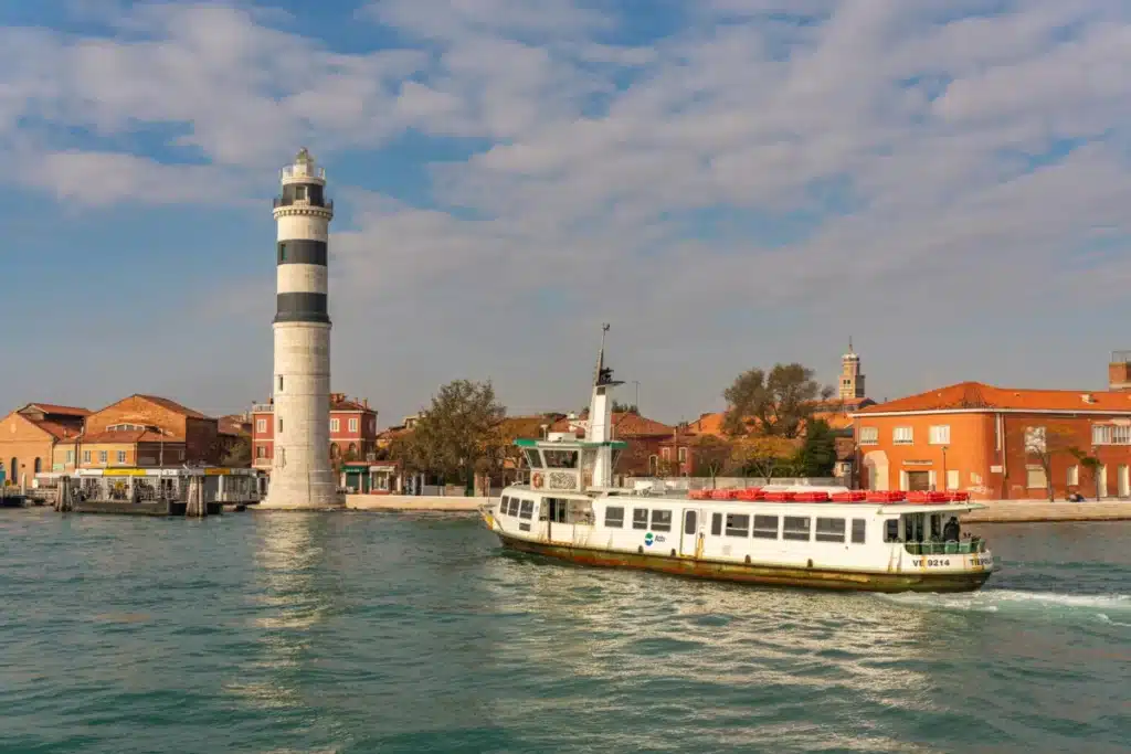 Île de Poveglia à Venise : le guide honnête d’une visite interdite Charming view of Murano with lighthouse and ferry sailing through Venetian waters.