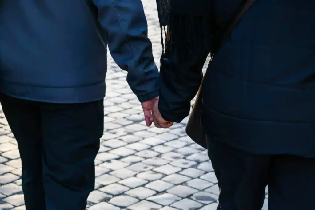 Évasion en couple à Rome antique : le guide honnête Back view of a couple holding hands walking on a cobblestone street.