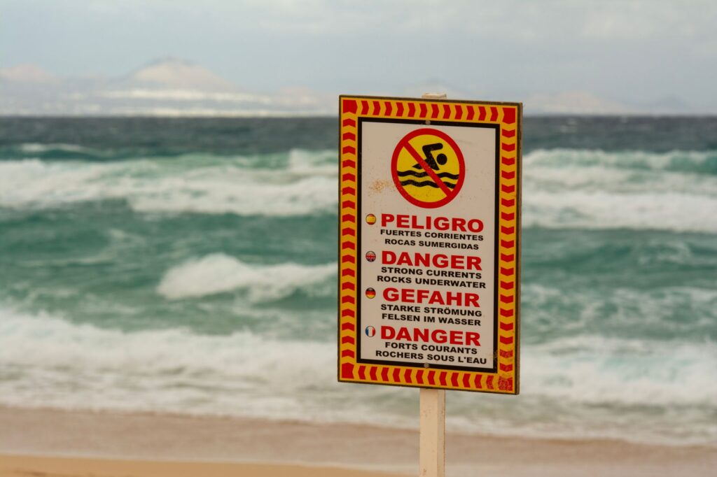 A beach warning sign cautioning about strong underwater currents in multiple languages.