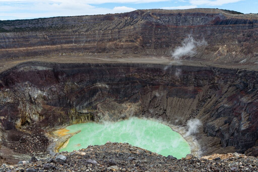 A breathtaking view of an active volcano crater with a vibrant sulfuric lake emitting steam under a clear sky.