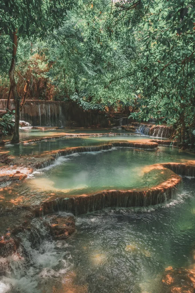 A breathtaking view of Kuang Si Falls surrounded by lush greenery in Luang Prabang, Laos.