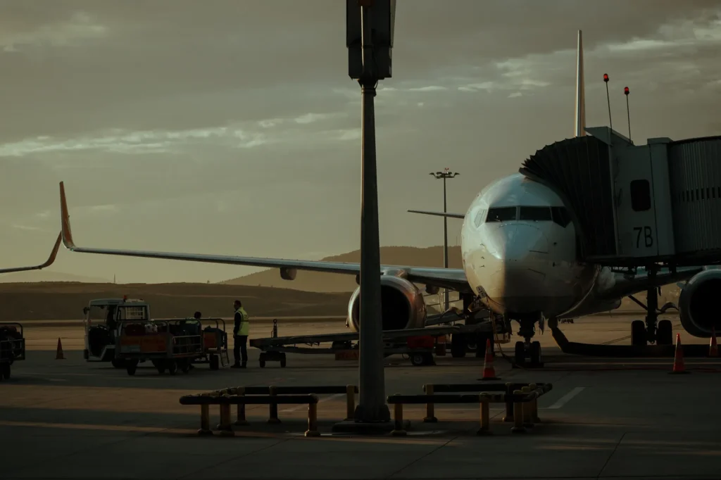 A commercial airplane at an airport gate during sunset with ground crew preparing for departure.