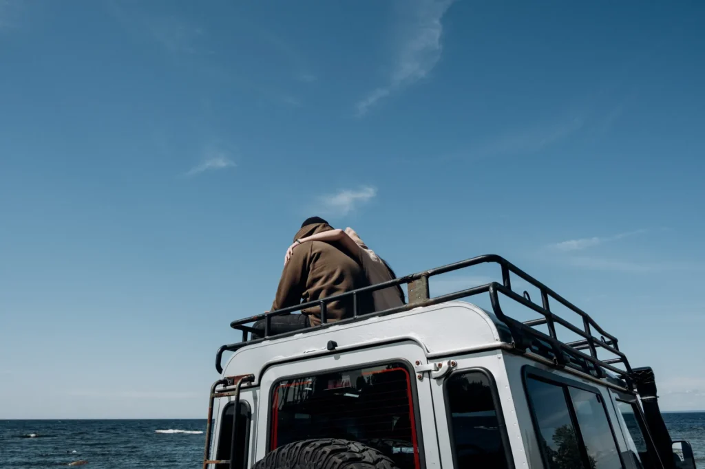 A couple enjoying a romantic moment on top of a rugged SUV by the sea under a clear blue sky.
