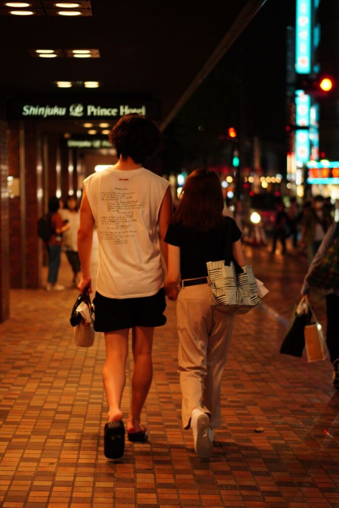 A couple holding hands on a busy street in Shinjuku, Tokyo at night.
