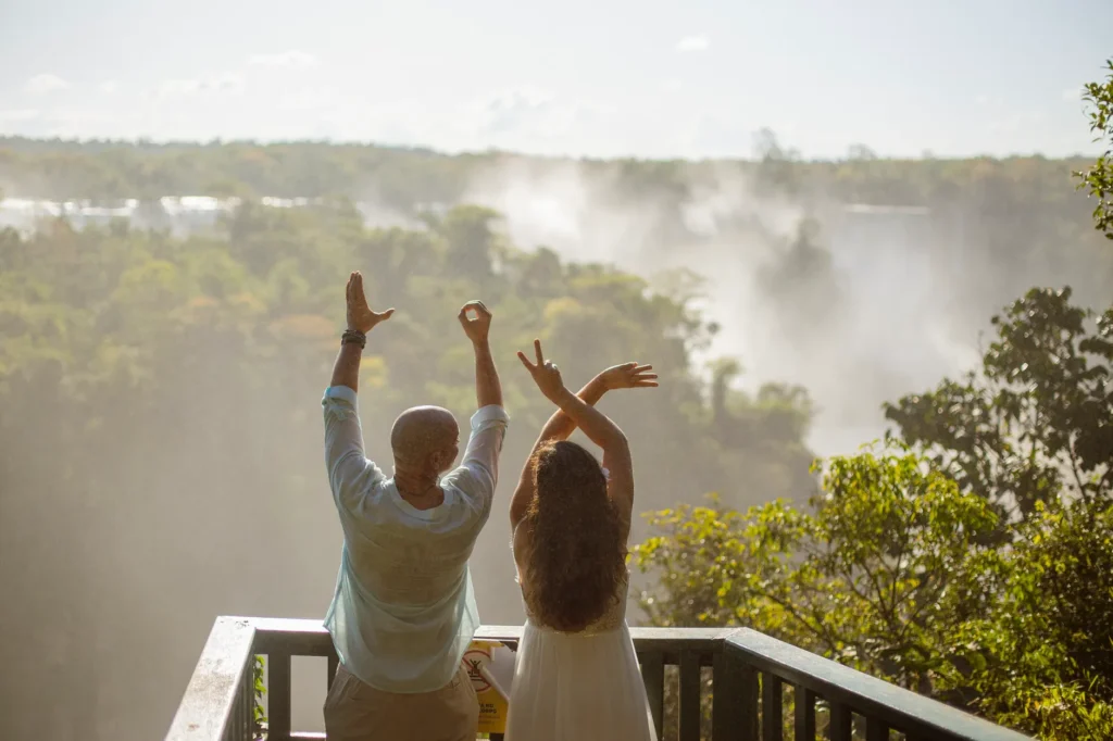 A couple raising arms embracing nature from a balcony at Iguazu Falls, Foz do Iguaçu.