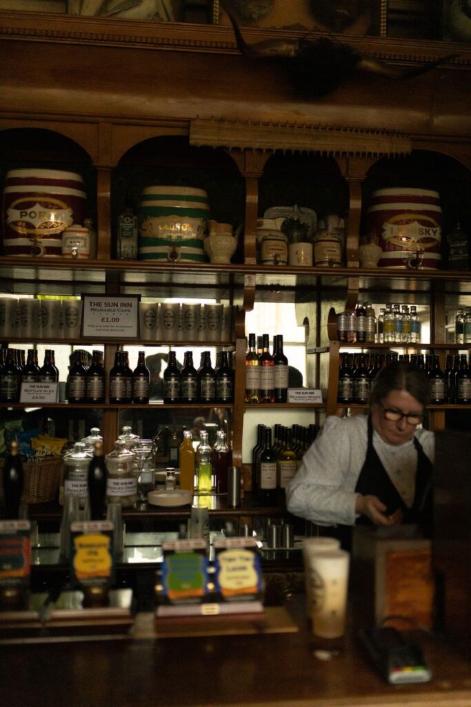 A cozy pub interior featuring vintage decor, a stocked bar, and a shop assistant at work.