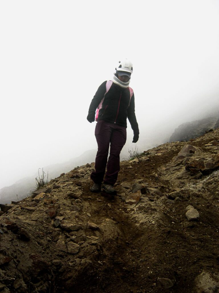 A female hiker with a helmet navigates a foggy mountain trail, showcasing adventure and nature.