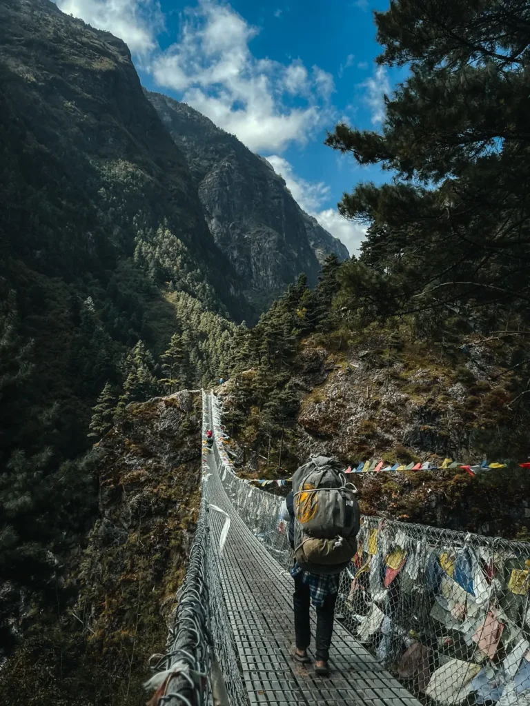 A hiker crosses a suspension bridge surrounded by stunning Himalayan views in Namche, Nepal.