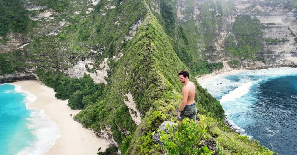 Nusa Penida en couple : se déplacer sans se cramer (scooter ou chauffeur, mode d’emploi) A man exploring steep cliffs at Kelingking Beach, Nusa Penida, Bali, offering breathtaking ocean views.