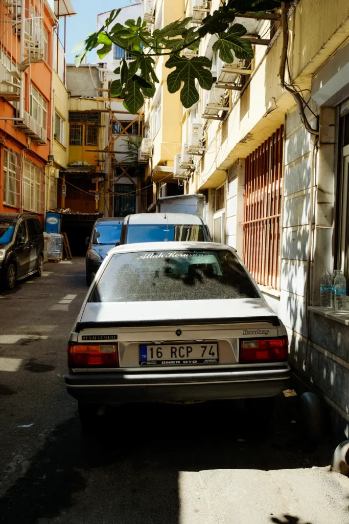 A narrow urban alleyway with parked cars, surrounded by tall residential buildings.