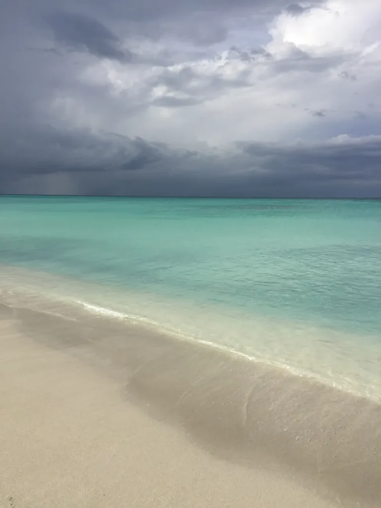 A serene beach scene with turquoise water under a dramatic, cloudy sky.