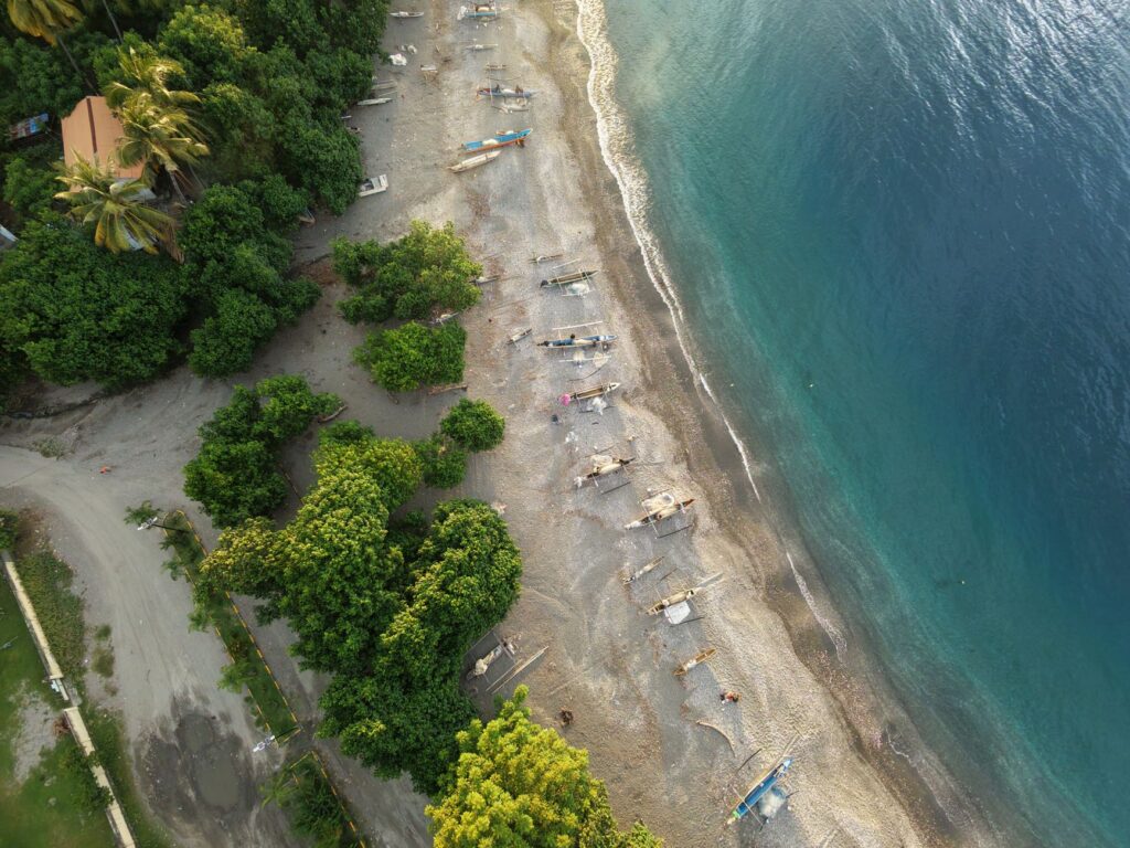 A stunning aerial view of a beach in Timor-Leste with fishing boats and lush greenery.