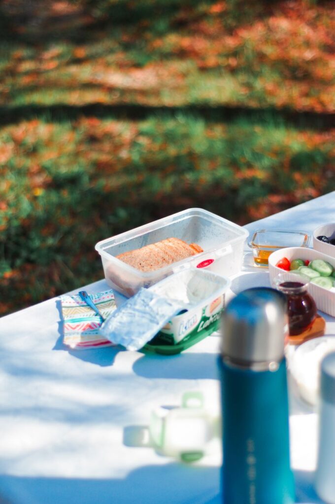 A vibrant outdoor picnic setup with sandwiches, thermos, and fresh veggies on a sunny day.