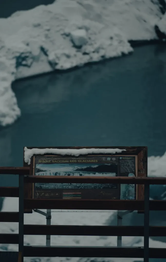 A view of a snow-covered sign overlooking a glacial lake in Los Glaciares National Park.