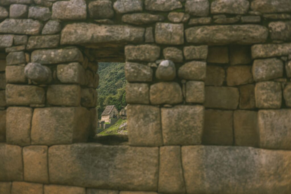 A view through a stone wall of the ancient ruins of Machu Picchu with lush greenery in the background.