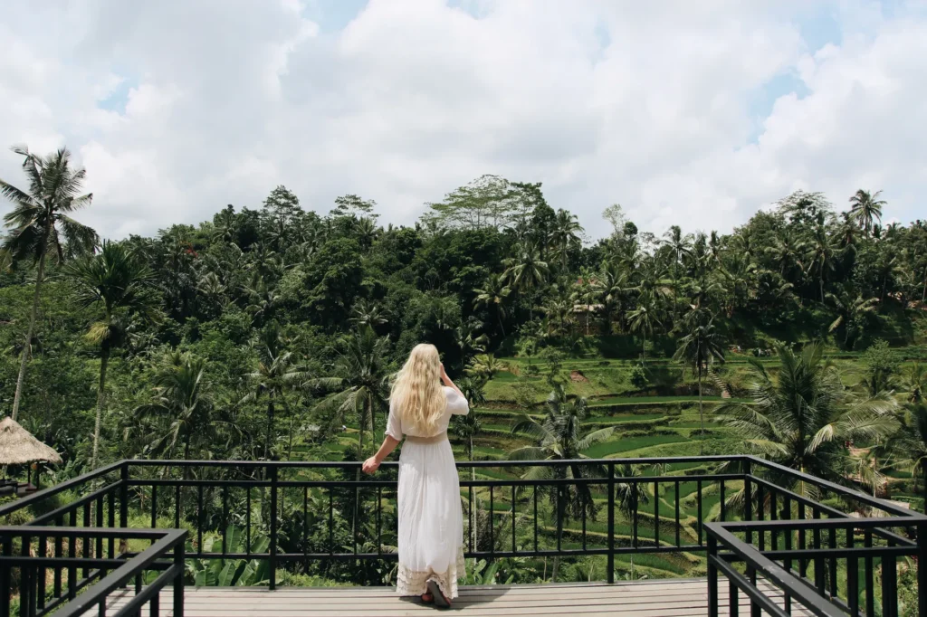 A woman with blonde hair overlooks a lush tropical forest from a balcony, capturing a serene and exotic travel moment.