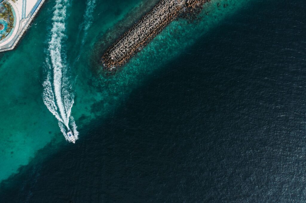 Aerial shot capturing a speedboat creating waves on clear turquoise waters alongside a scenic harbor.