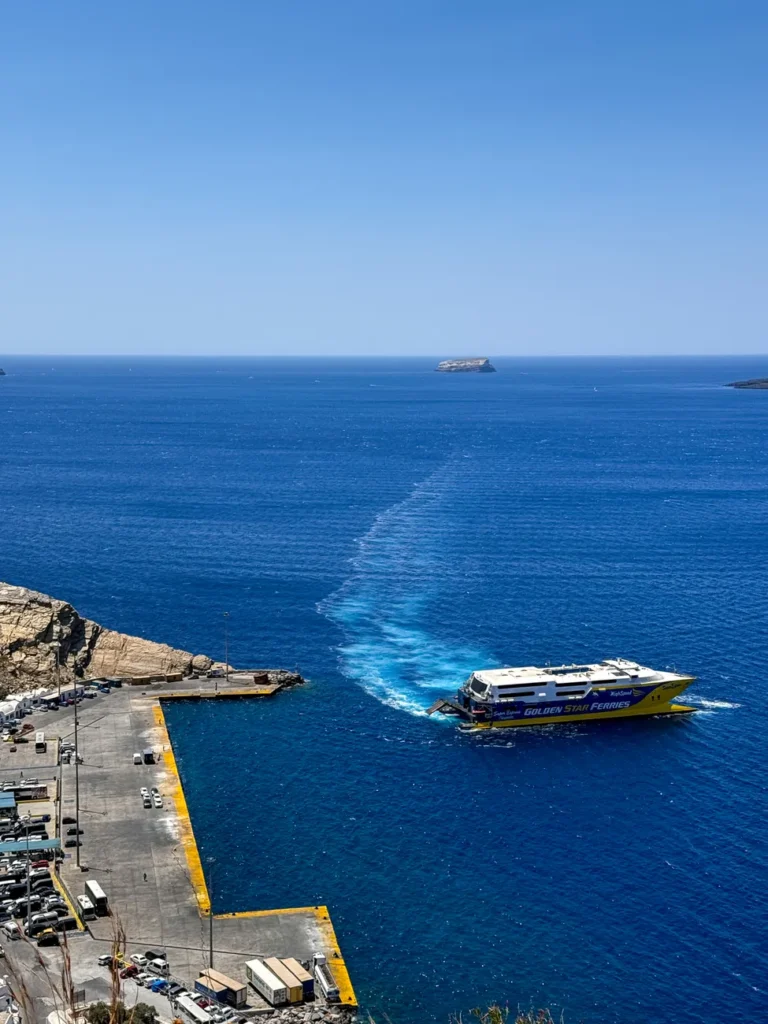 Aerial view of Blue Star Ferry leaving Fira harbour with deep blue sea in Santorini, Greece.
