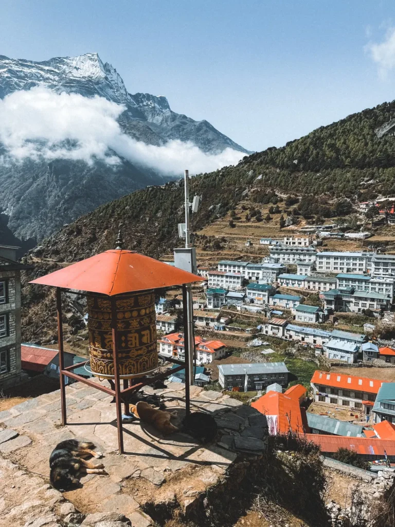 Aerial view of Namche Bazaar in Nepal with a traditional prayer wheel and mountain backdrop.