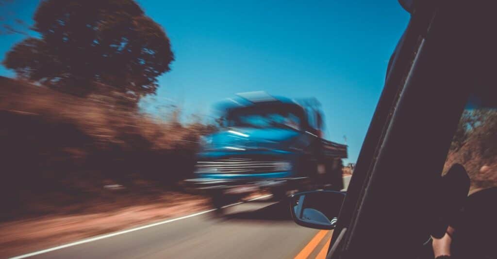 Location voiture au Brésil : guide à deux (prix, permis, conduite et pièges) Blurred motion of a blue truck speeding on a sunny highway, captured from a car window.
