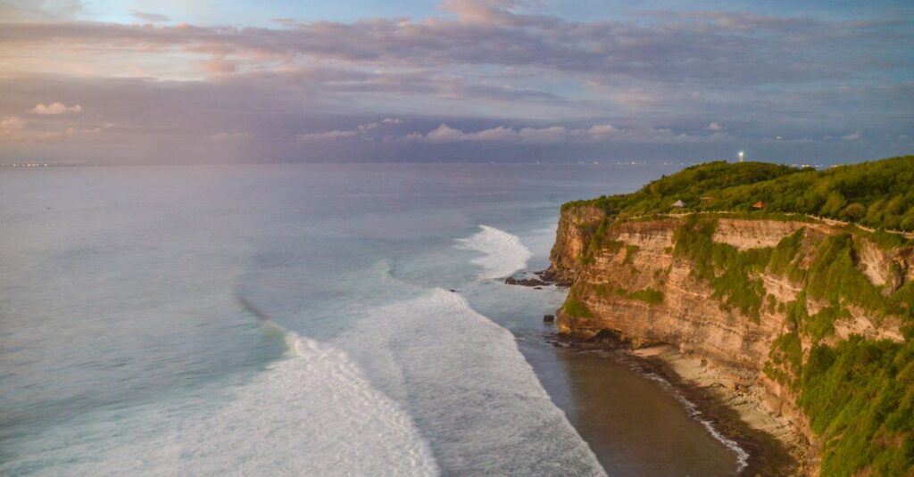 Uluwatu à deux : les plages qui font vraiment le job (sans finir en marathon d’escaliers) Breathtaking aerial view of Uluwatu cliffs in Bali with vibrant ocean waves during sunset.