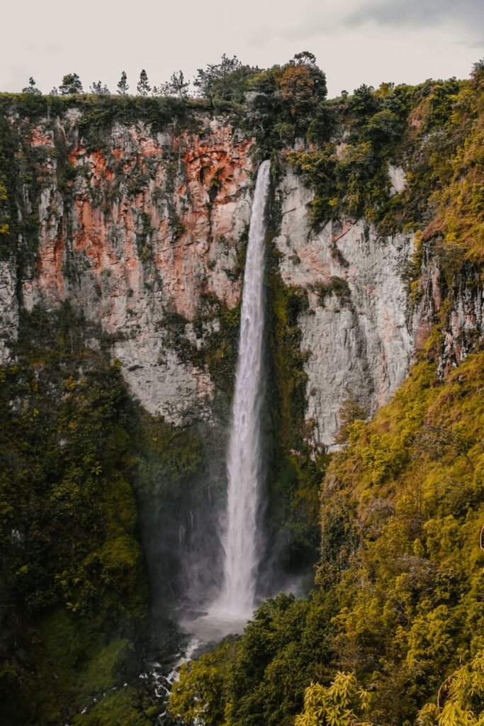 Breathtaking view of Sipiso-piso Waterfall cascading amidst lush greenery in North Sumatra, Indonesia.