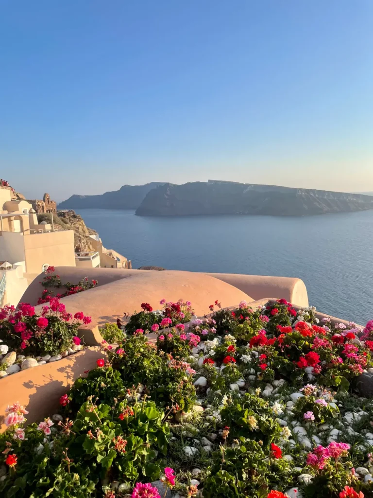 Captivating view of Oia, Santorini featuring iconic architecture, vibrant flowers, and the Aegean Sea at sunset.