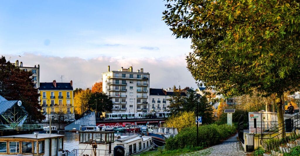 Voyages à Nantes : le city-break à deux qui sent bon la Loire Charming riverside view of Nantes, France, showcasing boats, buildings, and autumn scenery.
