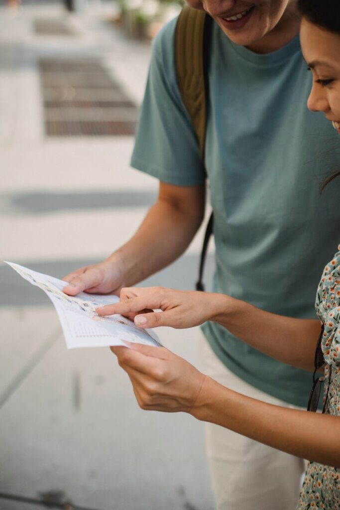 Cheerful crop anonymous couple pointing at location in map while exploring city during trip