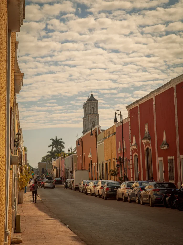Colorful colonial buildings line a street in Valladolid, Mexico, under a picturesque sky.