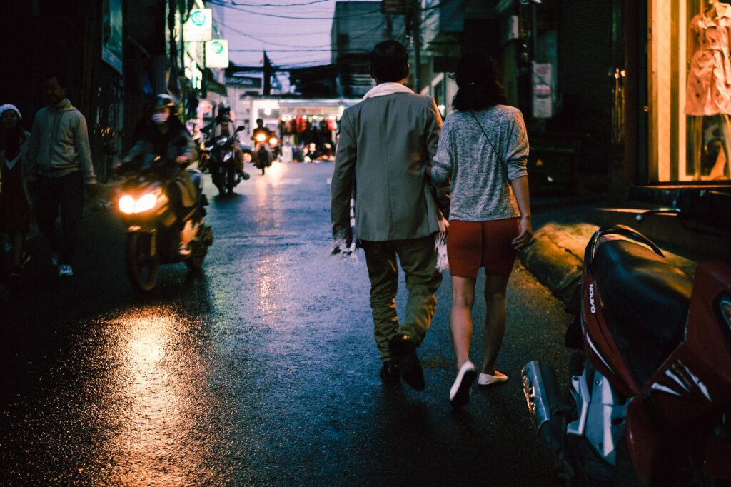 Couple strolling through city streets at night surrounded by motorcycles and urban lights.
