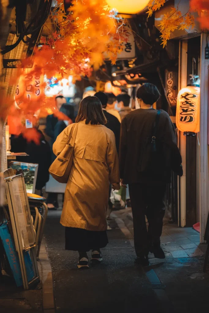 Couple walking through illuminated Omoide Yokocho, Tokyo at night.