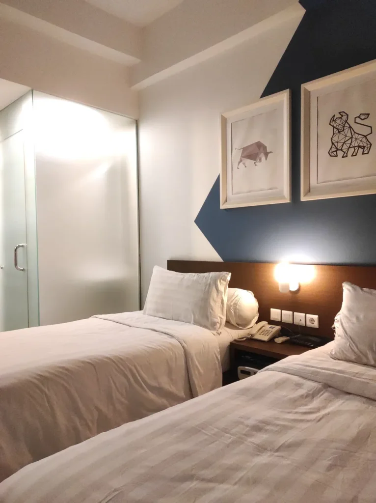 Cozy hotel room with twin beds, contemporary wall art, and soft lighting in urban setting.