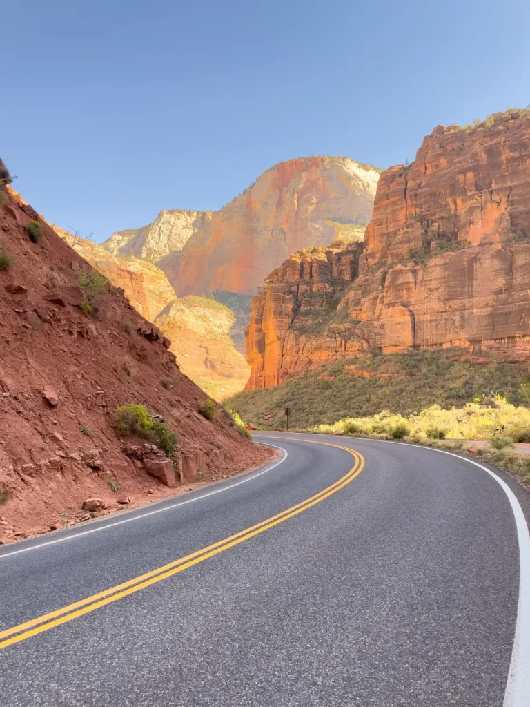 Curving road through dramatic red rock canyons in Zion National Park at daytime.