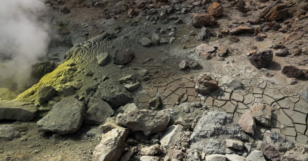 Dramatic view of a sulfur fumarole with cracked earth and rocky terrain, exuding geothermal steam.
