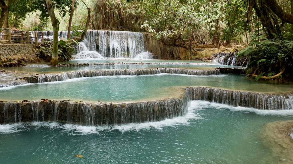 Explore the tranquil beauty of Kuang Si Waterfall with its turquoise waters surrounded by lush greenery.