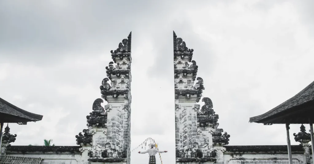 Pura Lempuyang à Bali : visiter les “portes du ciel” en couple, sans courir après le meilleur cliché Full length back view of unrecognizable person in traditional costume standing with arms outstretched standing at ancient gates of Pura Luhur Lempuyang Temple aka Gates of Heaven in Bali