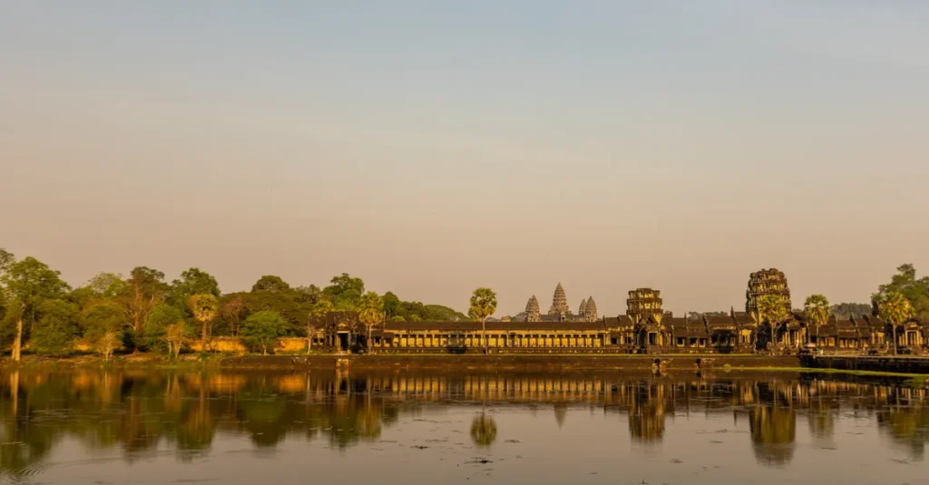 Majestic Angkor Wat temple reflecting in calm waters at sunrise, showcasing ancient architecture.