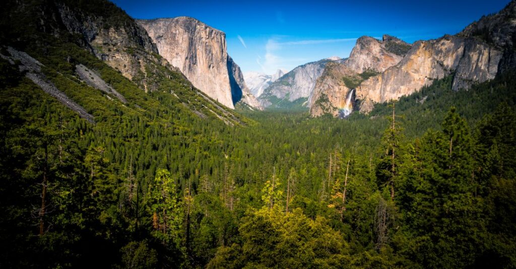 Yosemite à deux : l’itinéraire d’une journée qui tient la route (et les plus beaux spots) Majestic view of Yosemite Valley with lush forests, cliffs, and waterfalls under a clear blue sky.