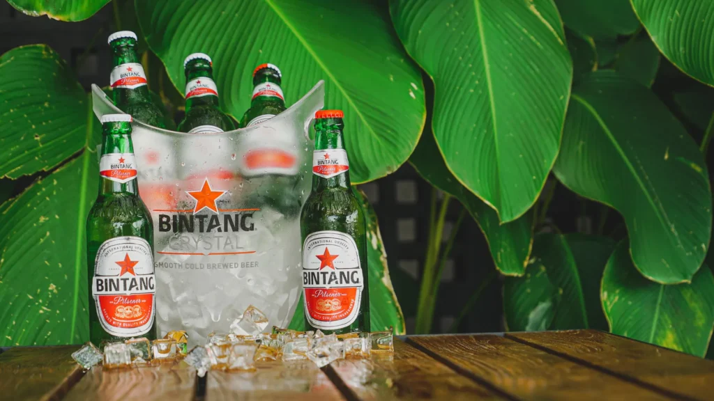 Refreshing Bintang beer bottles on a table with ice, framed by lush green leaves.