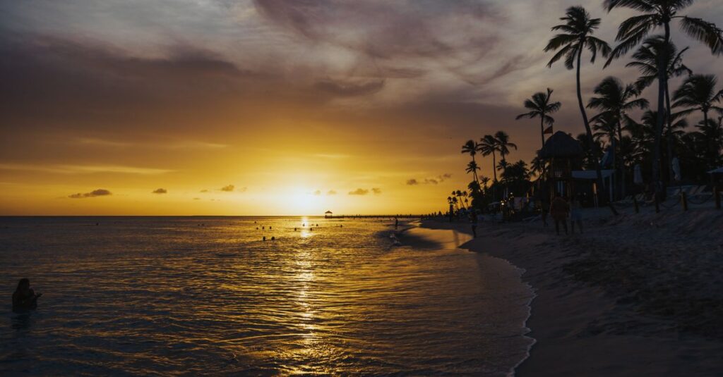 Serene tropical beach at sunset, with palm trees silhouetted against a golden sky, reflecting on calm waves.
