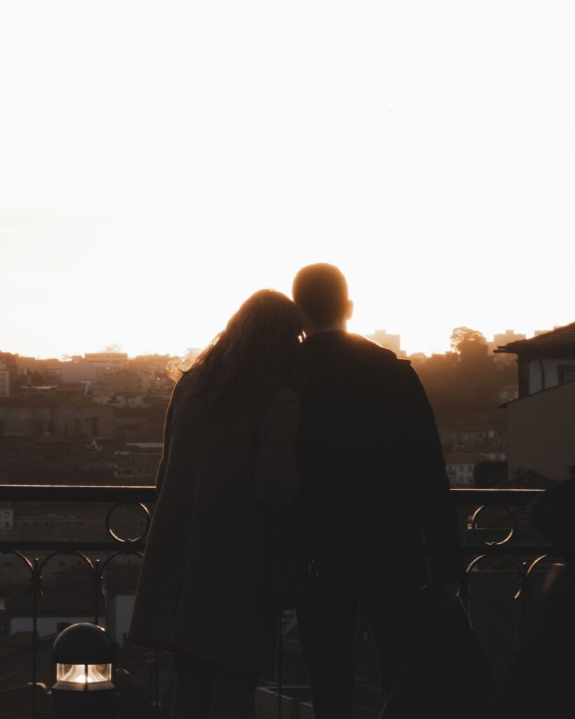 Silhouette of a couple embracing on a balcony during sunrise, with cityscape views.