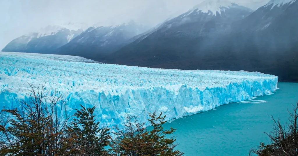 Perito Moreno en couple : guide concret pour marcher sur la glace (Patagonie) Snow-covered Perito Moreno Glacier majestically extending into turquoise waters, surrounded by snow-capped mountains.