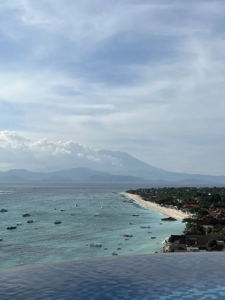 Stunning view of Bali's coastline with boats on the turquoise sea and a mountain backdrop.