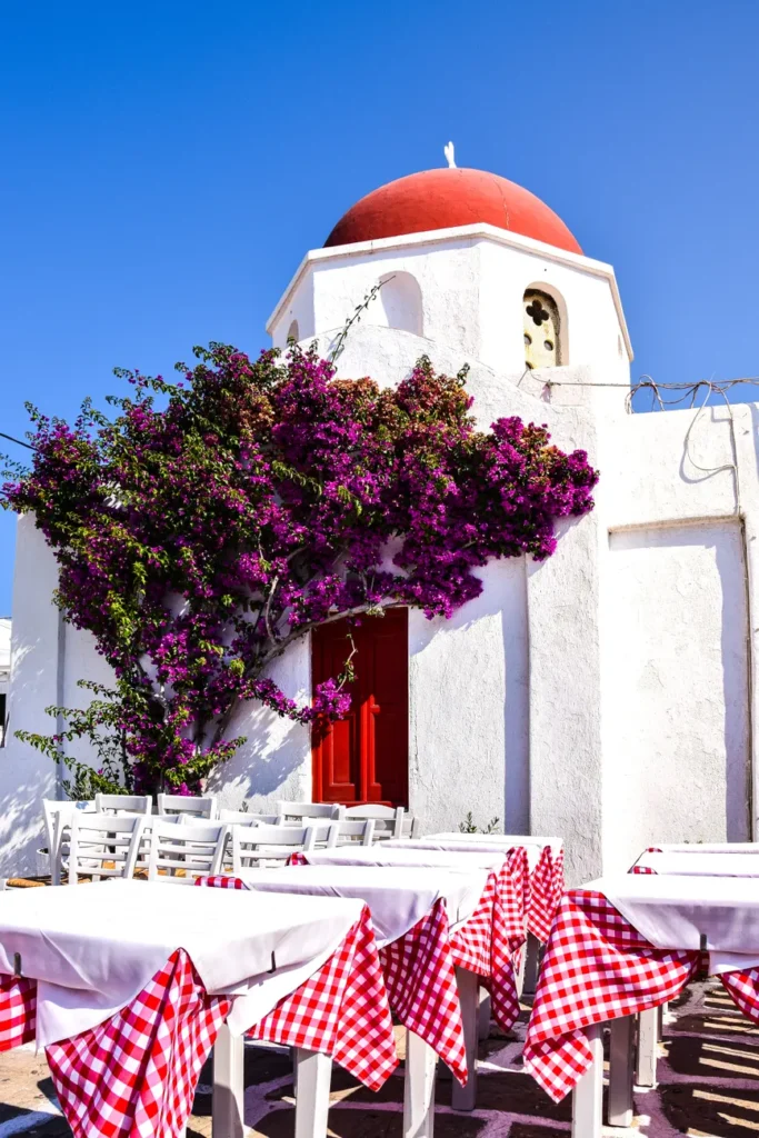 Sunlit Greek taverna with vibrant bougainvillea and classic architecture.