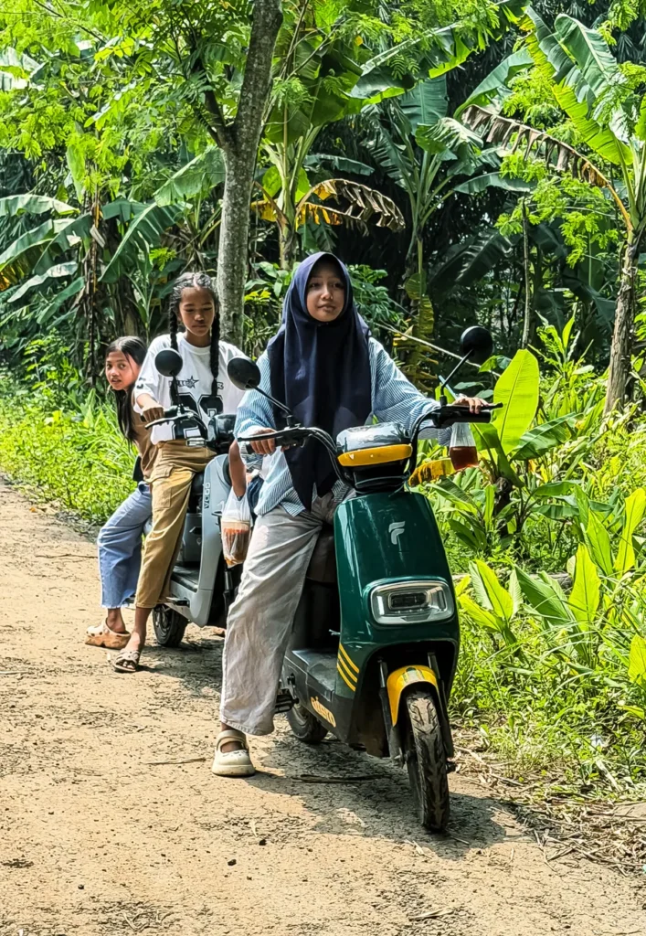 Three young women on scooters ride through a vibrant jungle path, enjoying an adventurous day outdoors.
